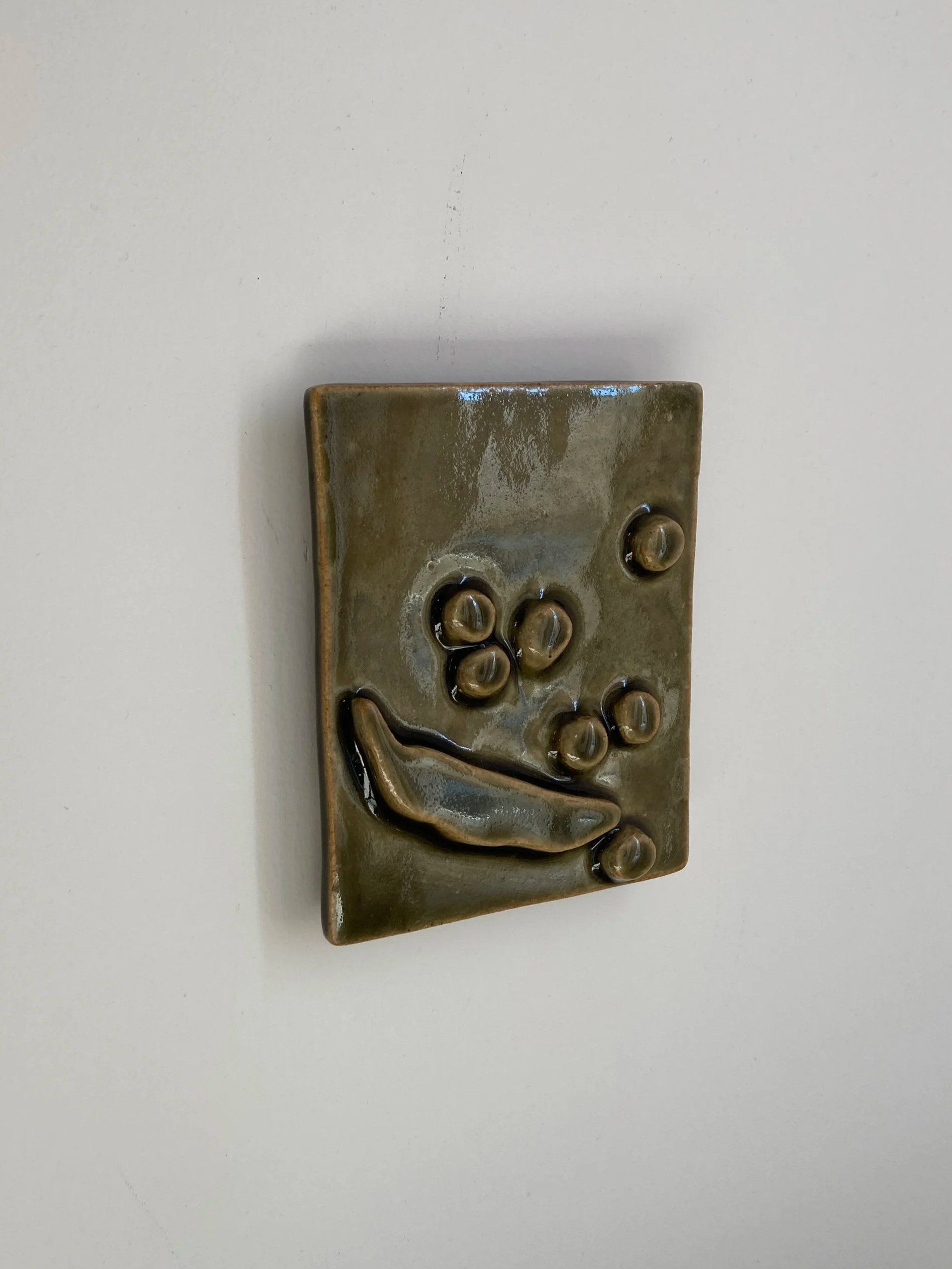 Un bas-relief mural de céramique accroché au mur, représentant un haricot et des petits pois.