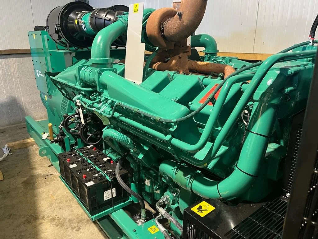 Large industrial diesel engine with green casing and exhaust pipes in a workshop.