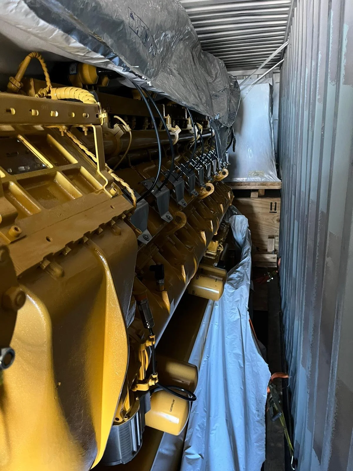 Large yellow industrial machinery partially covered in a tarp inside a container.