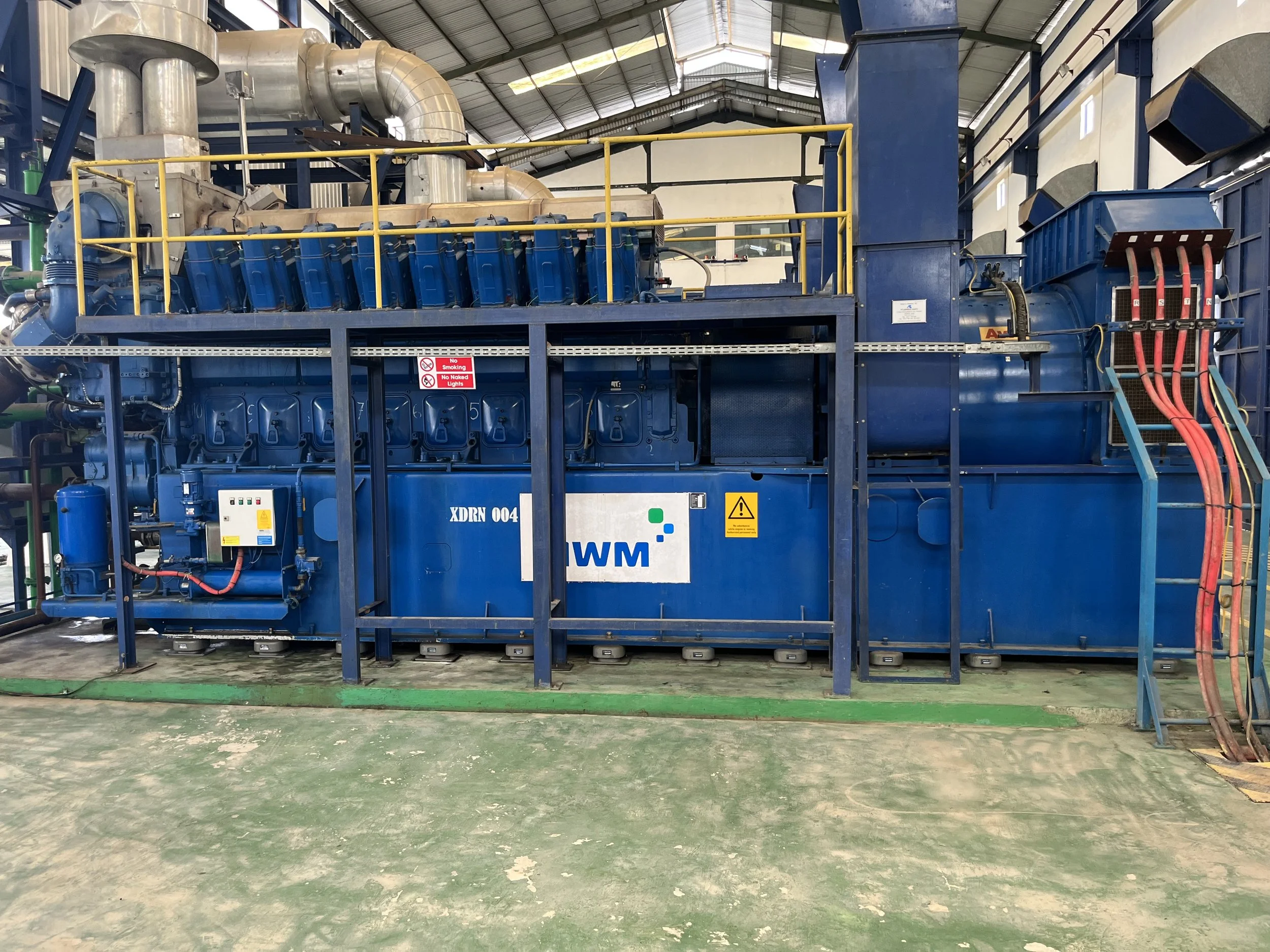 Industrial machinery, possibly a large engine or generator, with blue exterior and pipes in a factory setting.