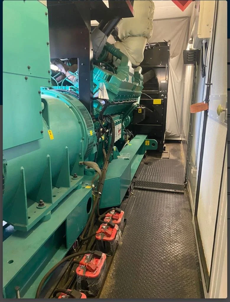 Industrial generator with attached cables and batteries inside a metal-floored room.