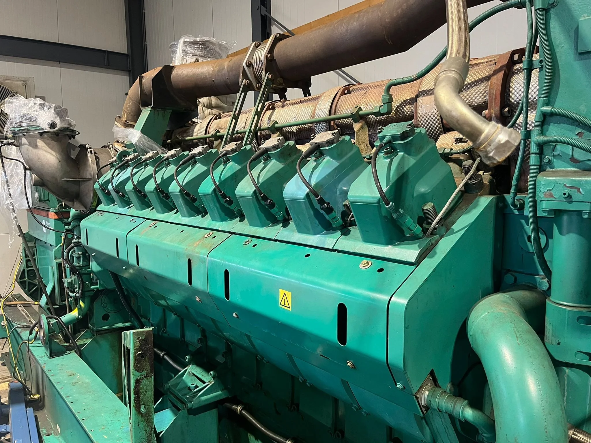 Industrial diesel engine with green casing and multiple cylinders in a factory setting.