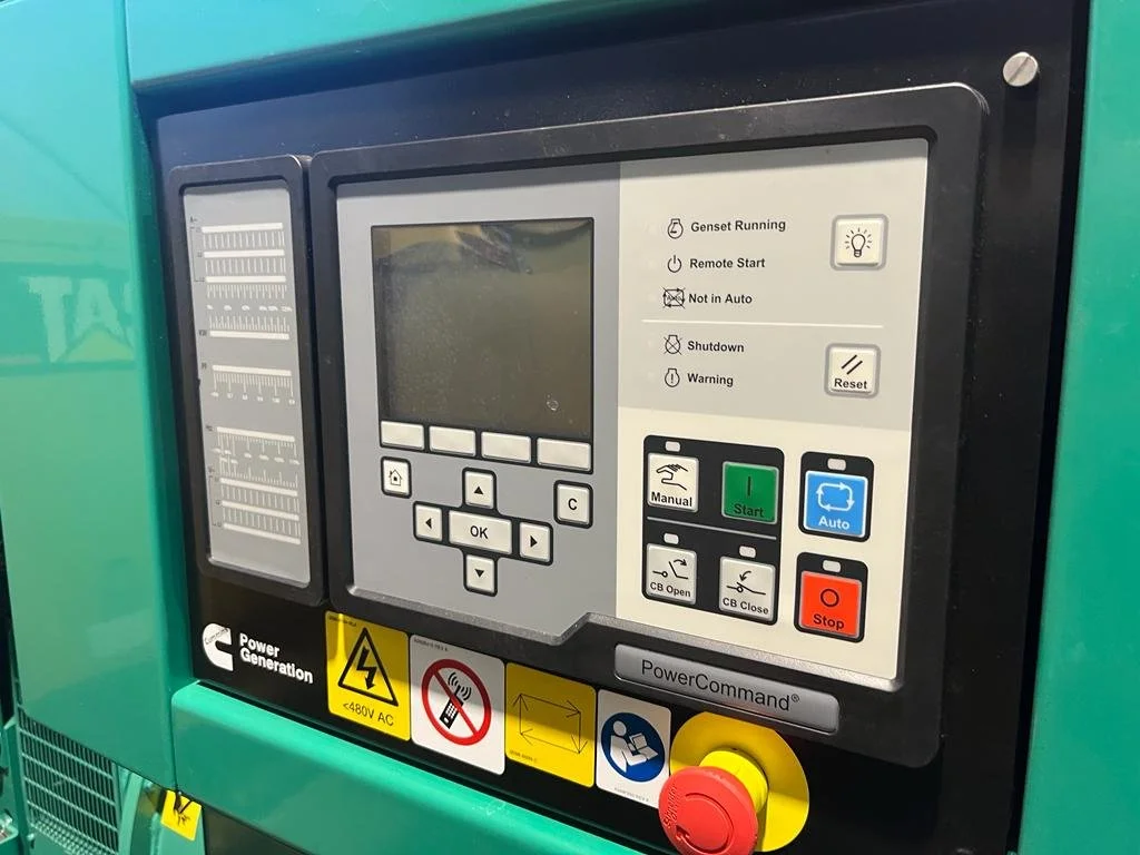 Close-up of a generator control panel with various buttons and indicators, including start, stop, manual and auto modes, and warning lights. The PowerCommand® logo is visible.