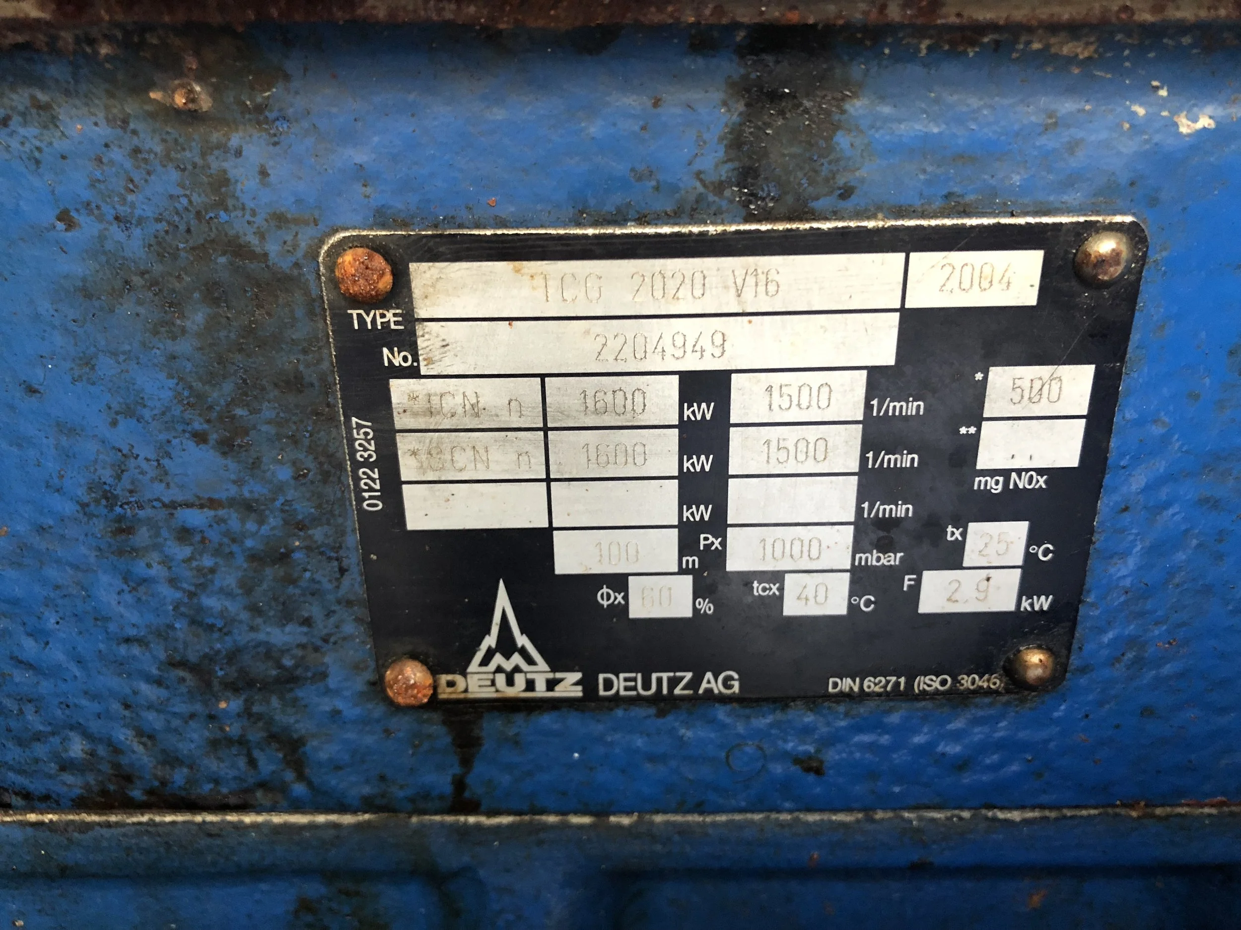 Close-up of a metal nameplate on a blue industrial machine, showing technical specifications such as type TCG 2020 V16, power ratings, and manufacturer Deutz AG.