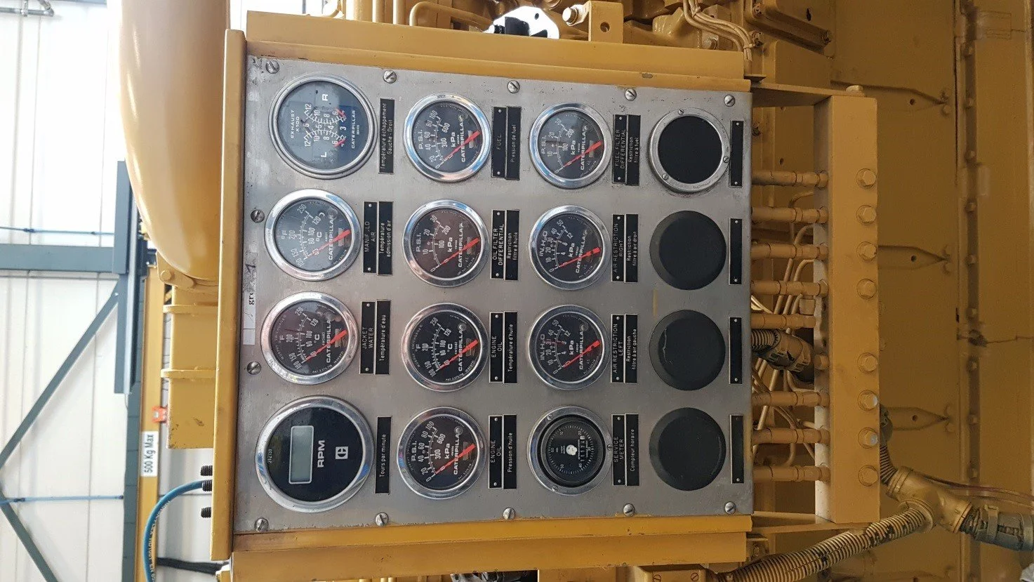 Control panel with multiple gauges and indicators, showing measurements such as PSI and RPM, likely part of industrial equipment or machinery, with dials and labels visible against a metallic background.