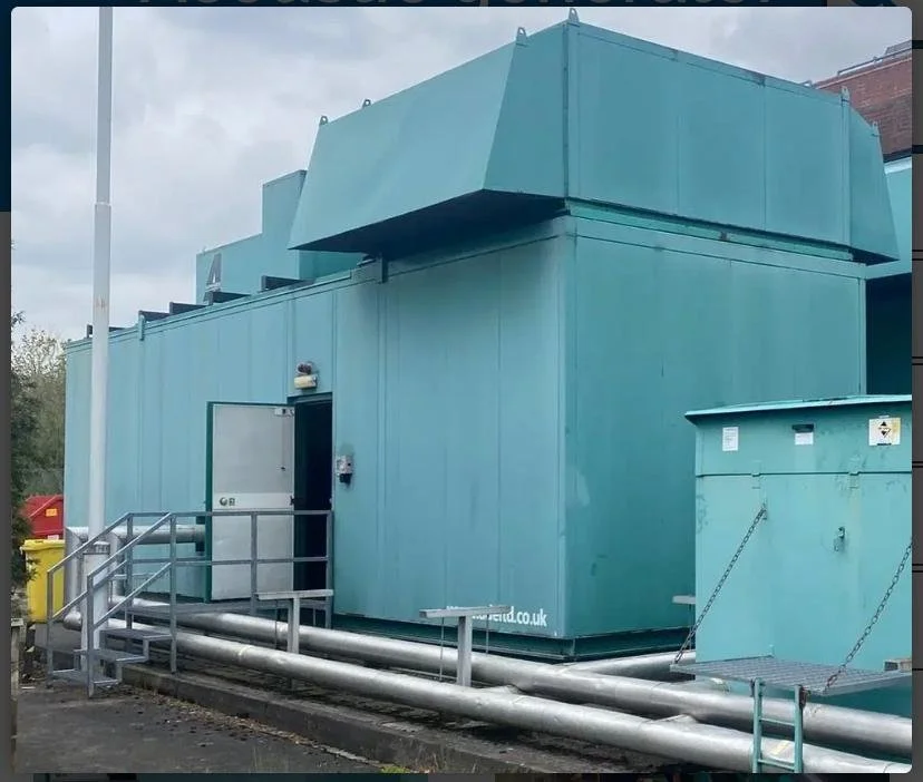 Large teal industrial structure with stairs and pipes outside.