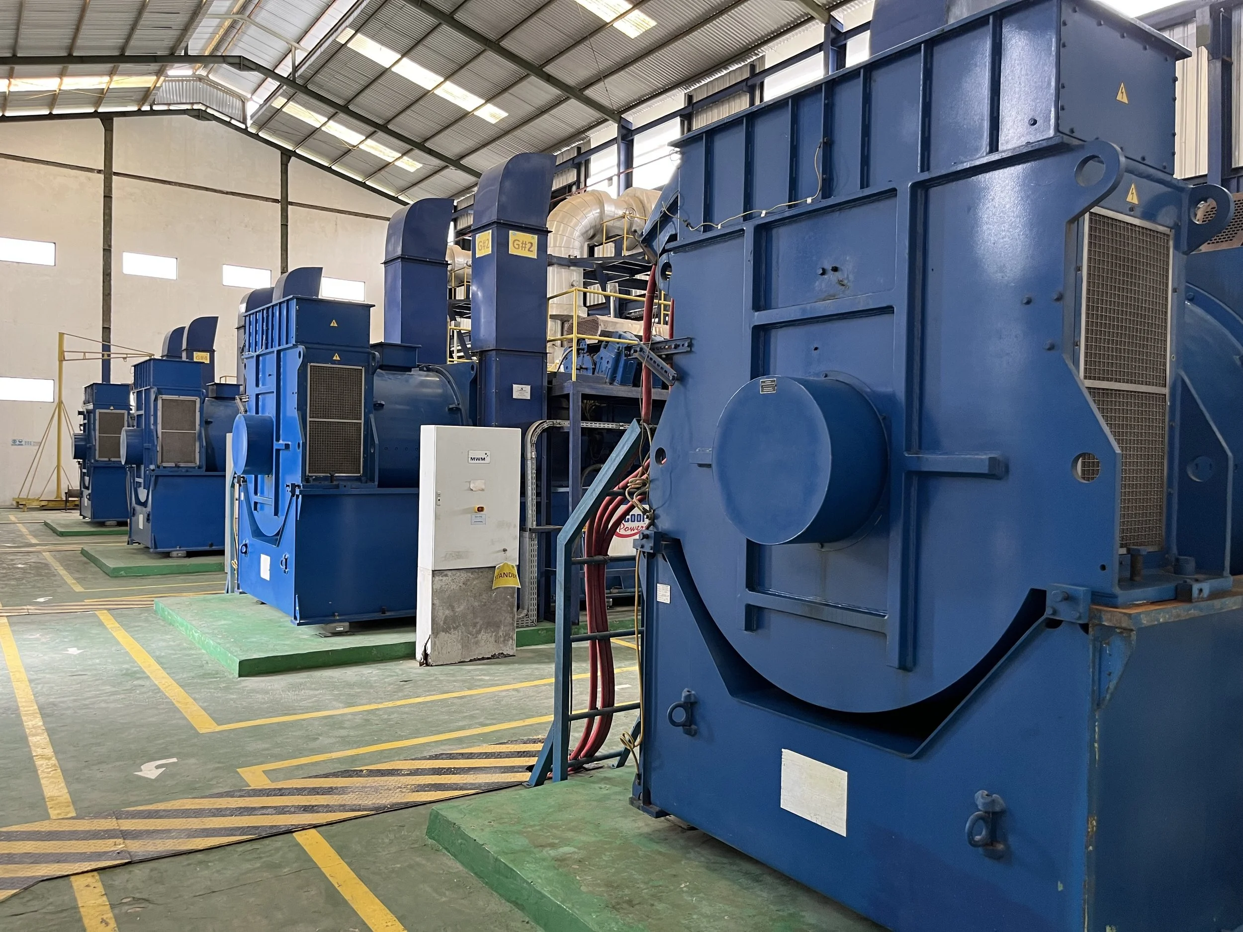 Industrial machinery in a factory with large blue machines arranged in a row and a high ceiling.