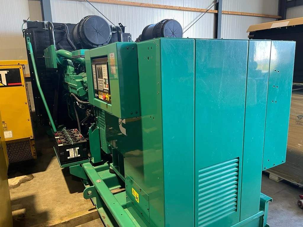 Industrial diesel generator in a warehouse, featuring a green metal casing and an electronic control panel.