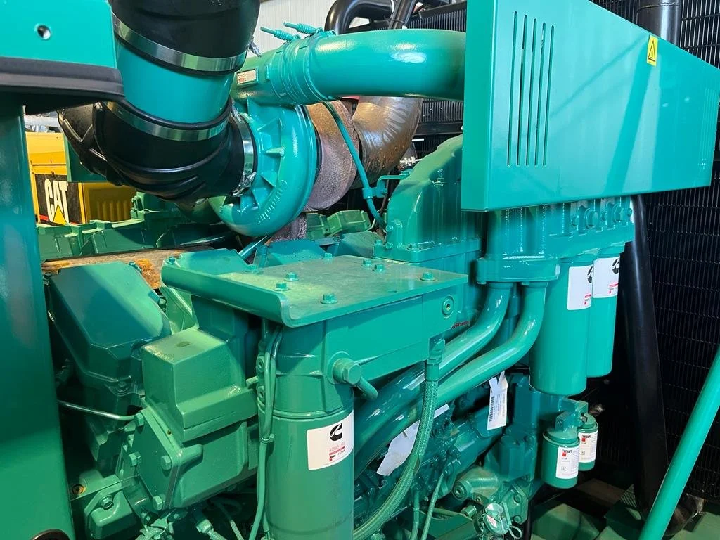 Close-up of a green industrial engine with pipes, filters, and labeled components. The background features a yellow CAT sign.