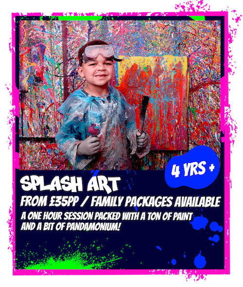 A young child with glasses and a painted shirt holding a paintbrush in a colorful splatter art studio.