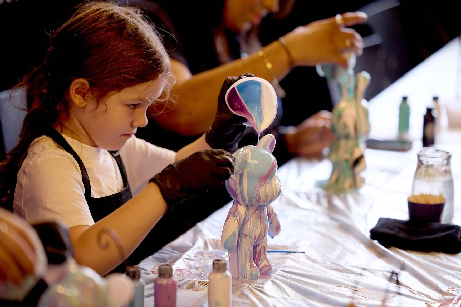 Young girl decorating a ceramic bear figurine with colorful paint at an art studio.