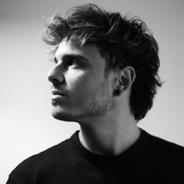Retrato en blanco y negro de un hombre joven con cabello rizado, barba corta y camiseta negra
