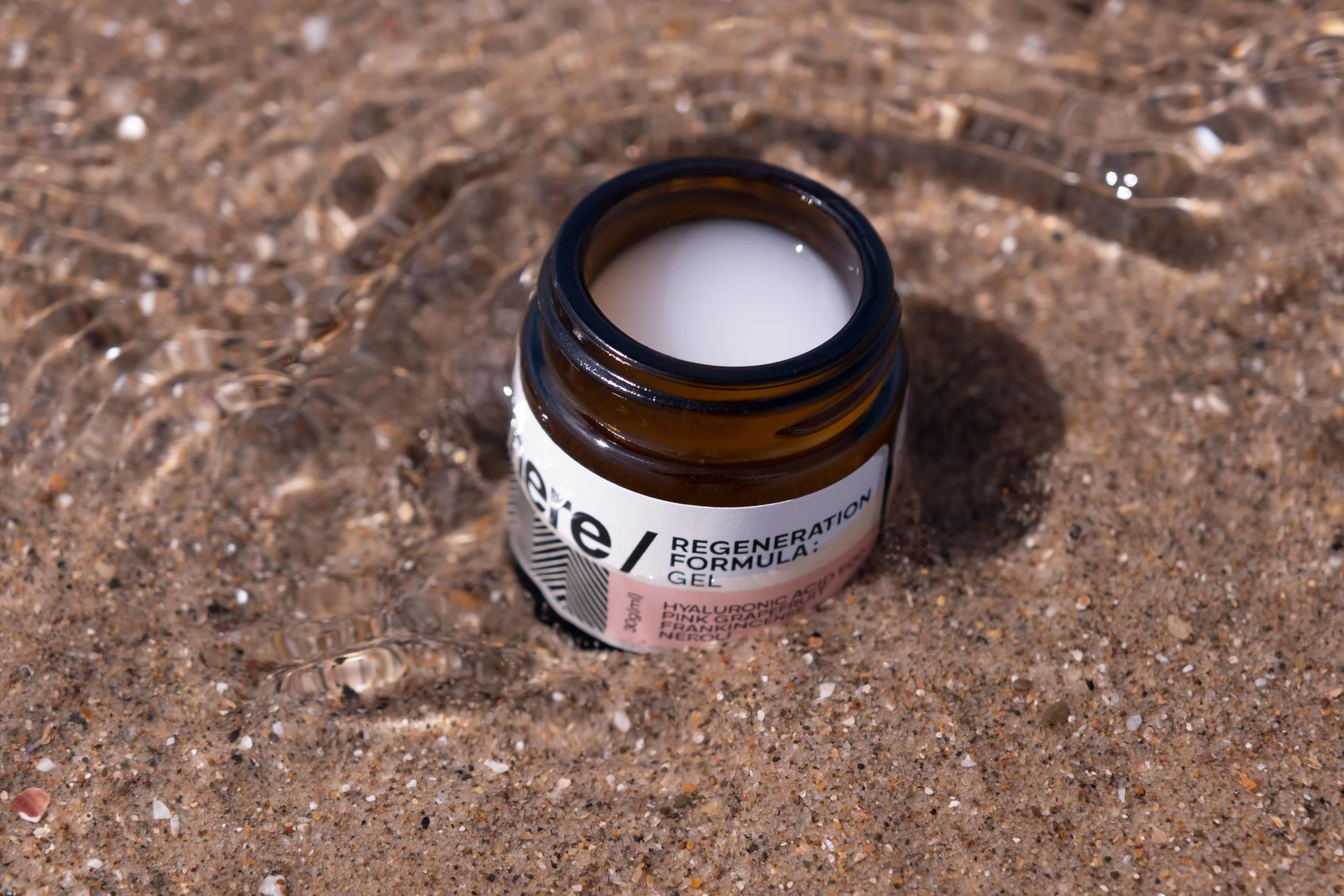 A black jar labeled 'elsewhere / Regeneration Formula: Gel' surrounded by green leaves and white flowers.