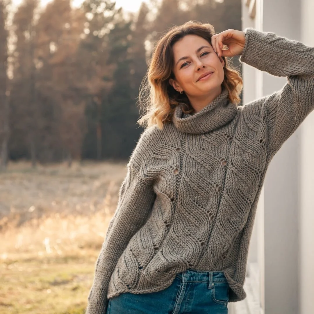 Woman in gray sweater smiling confidently while relaxing outdoors in warm afternoon sunlight.