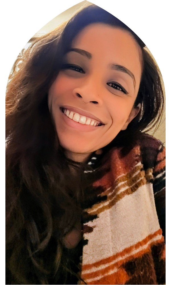A woman with long dark hair, a septum piercing, and a big smile showing her teeth, wearing a patterned scarf.