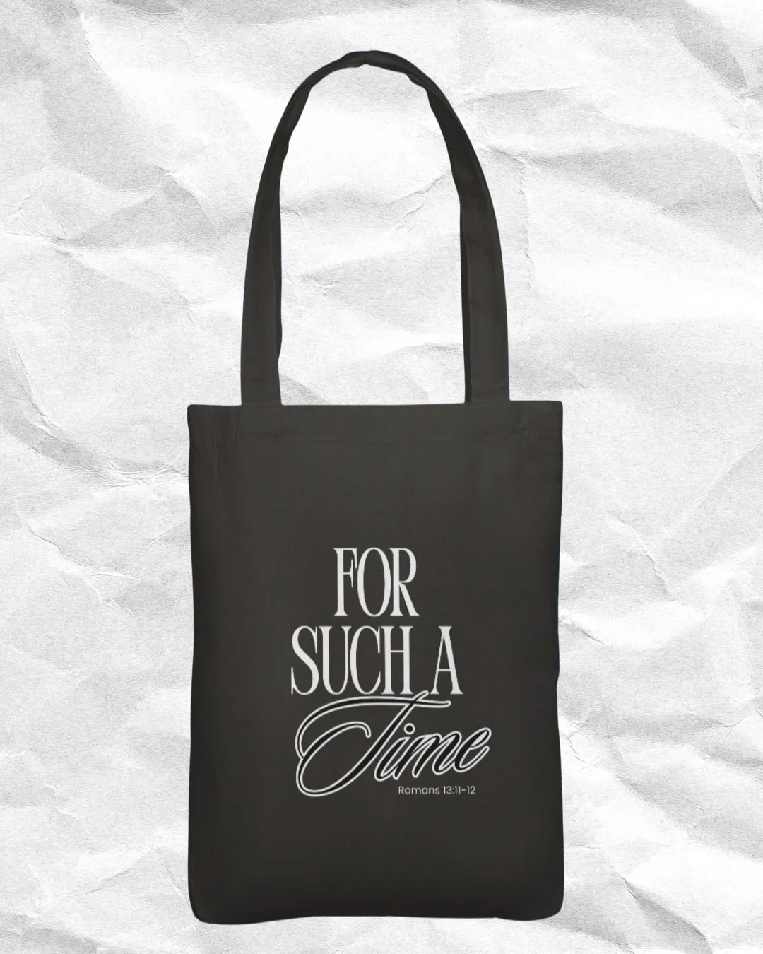 Black tote bag with white text reading "For Such A Time Romans 13:11-12" on a crumpled white background.