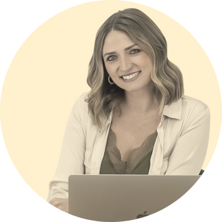 Kerrie Luginbill: A woman with shoulder-length wavy hair smiling, wearing a light-colored blazer over a white top, against a cream-colored background.