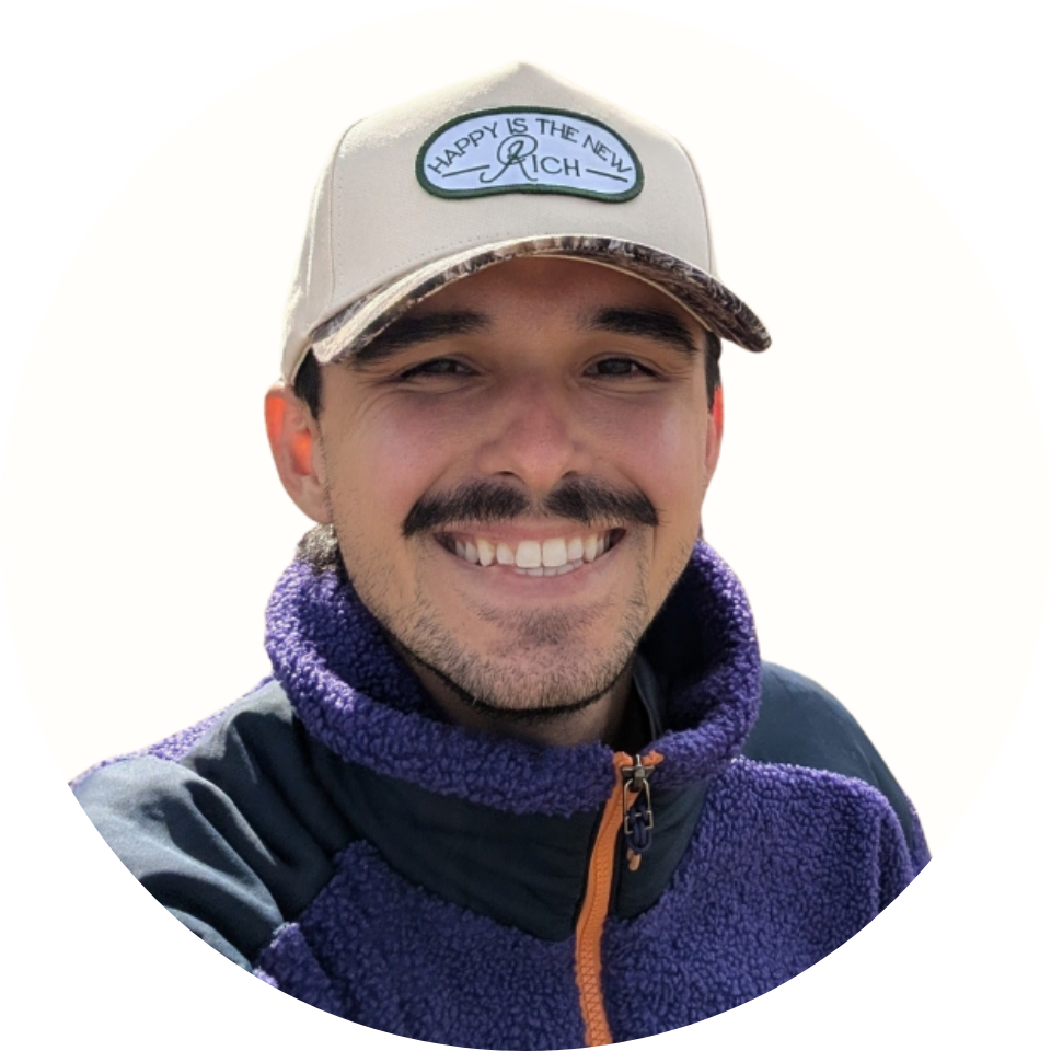 Smiling man wearing a beige cap with the phrase 'Happy is the new rich' and a purple fleece jacket.