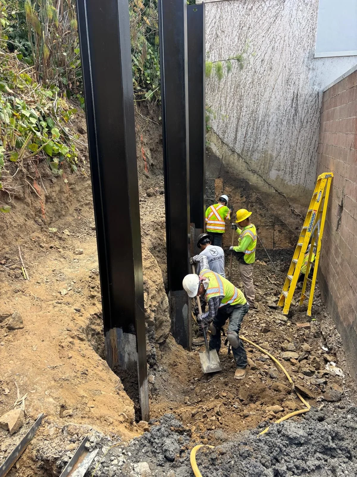 Manual excavation between beams in preparation for lagging board installation.