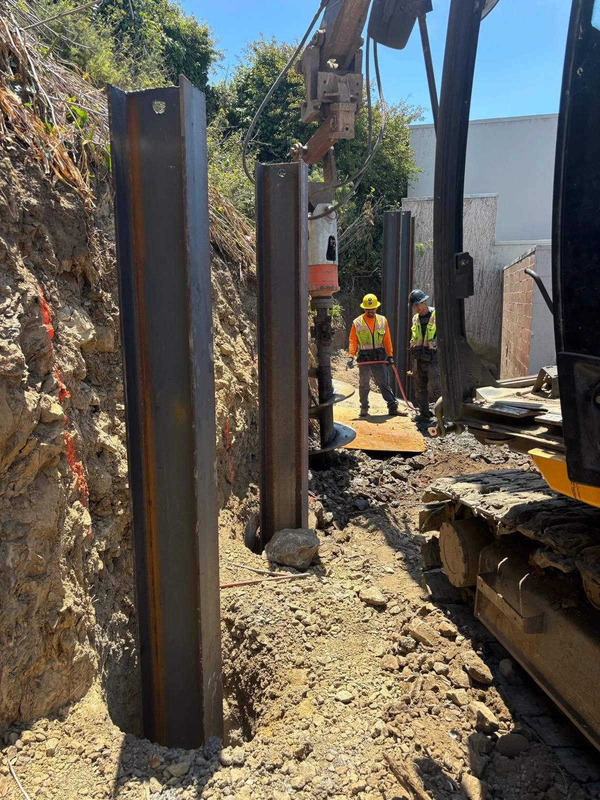 Beams being set into pre-drilled holes for retaining wall support.