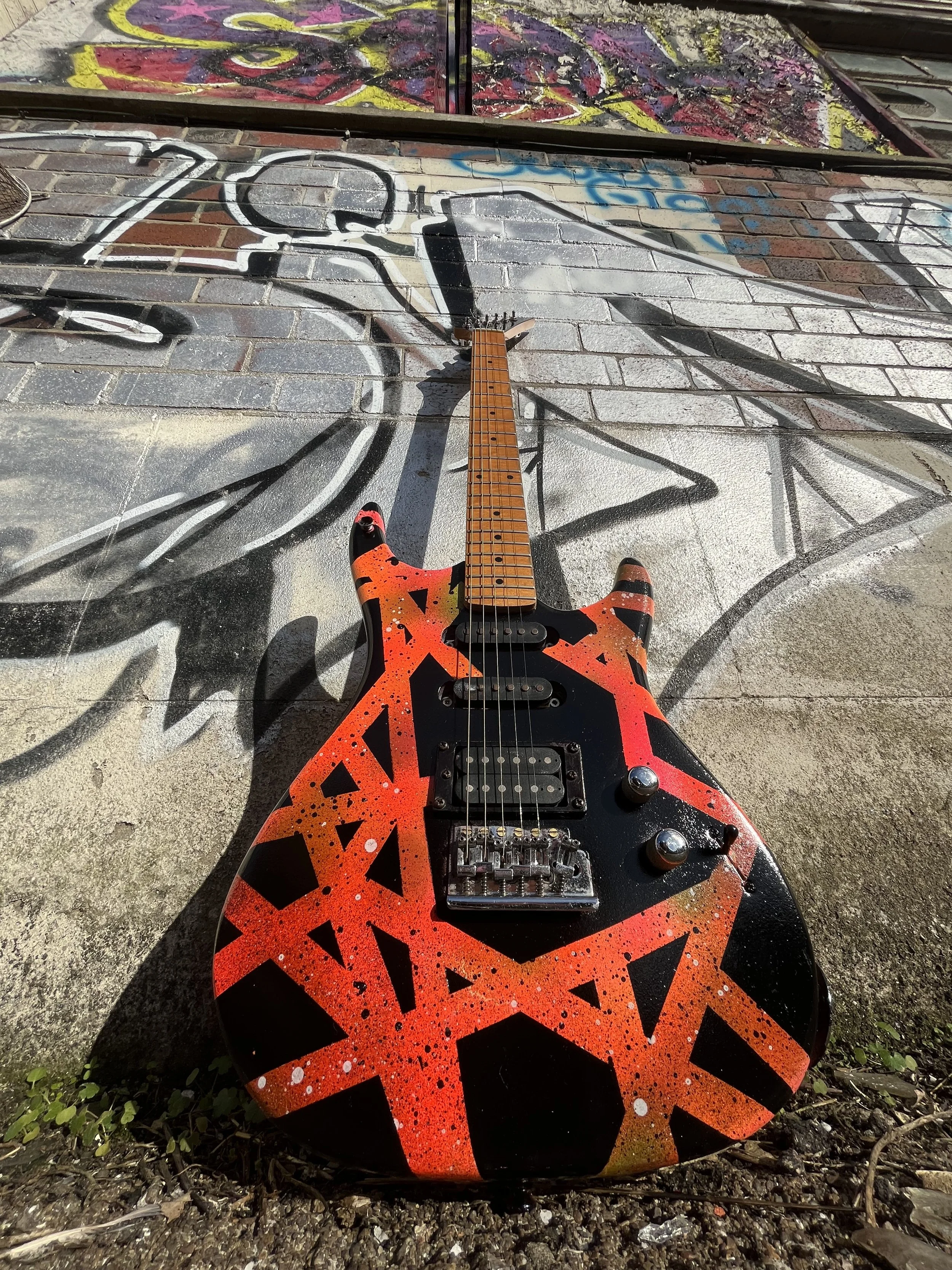 Electric guitar with red and black geometric design leaning against a graffiti-covered brick wall.