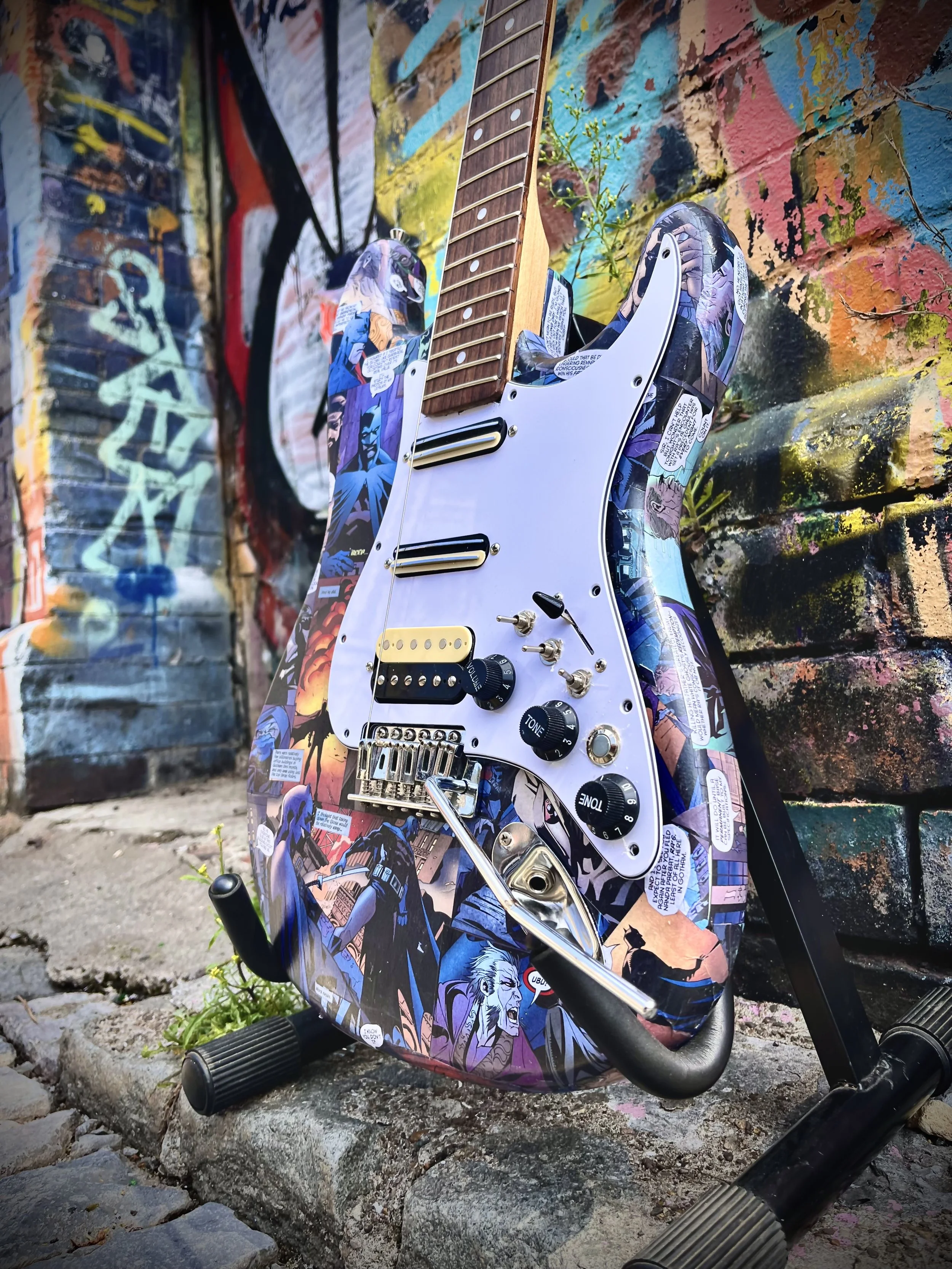 Electric guitar with comic book design on body, set against a graffiti-covered wall.