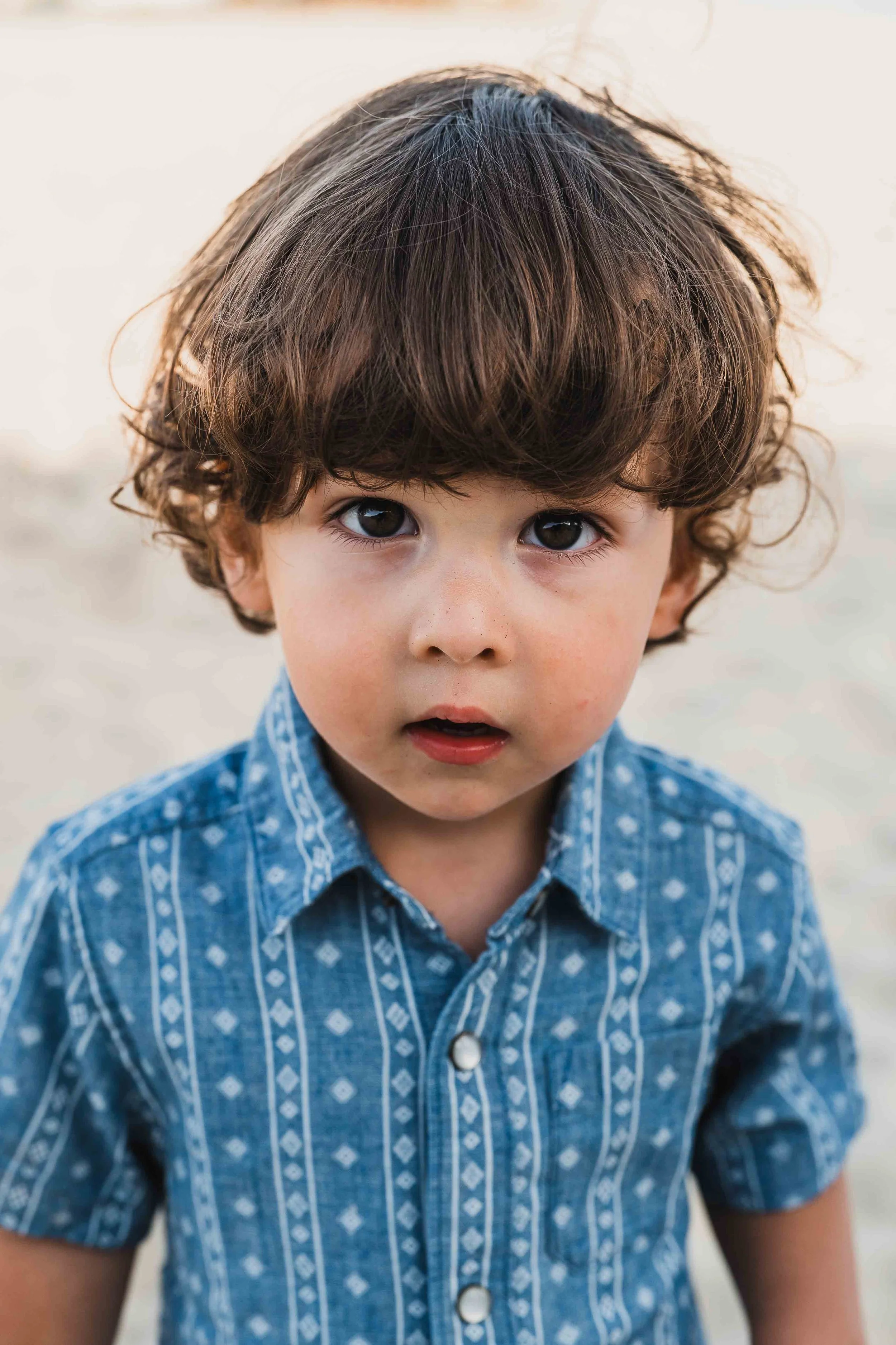 little boy in blue shirt on beach looking right at camera