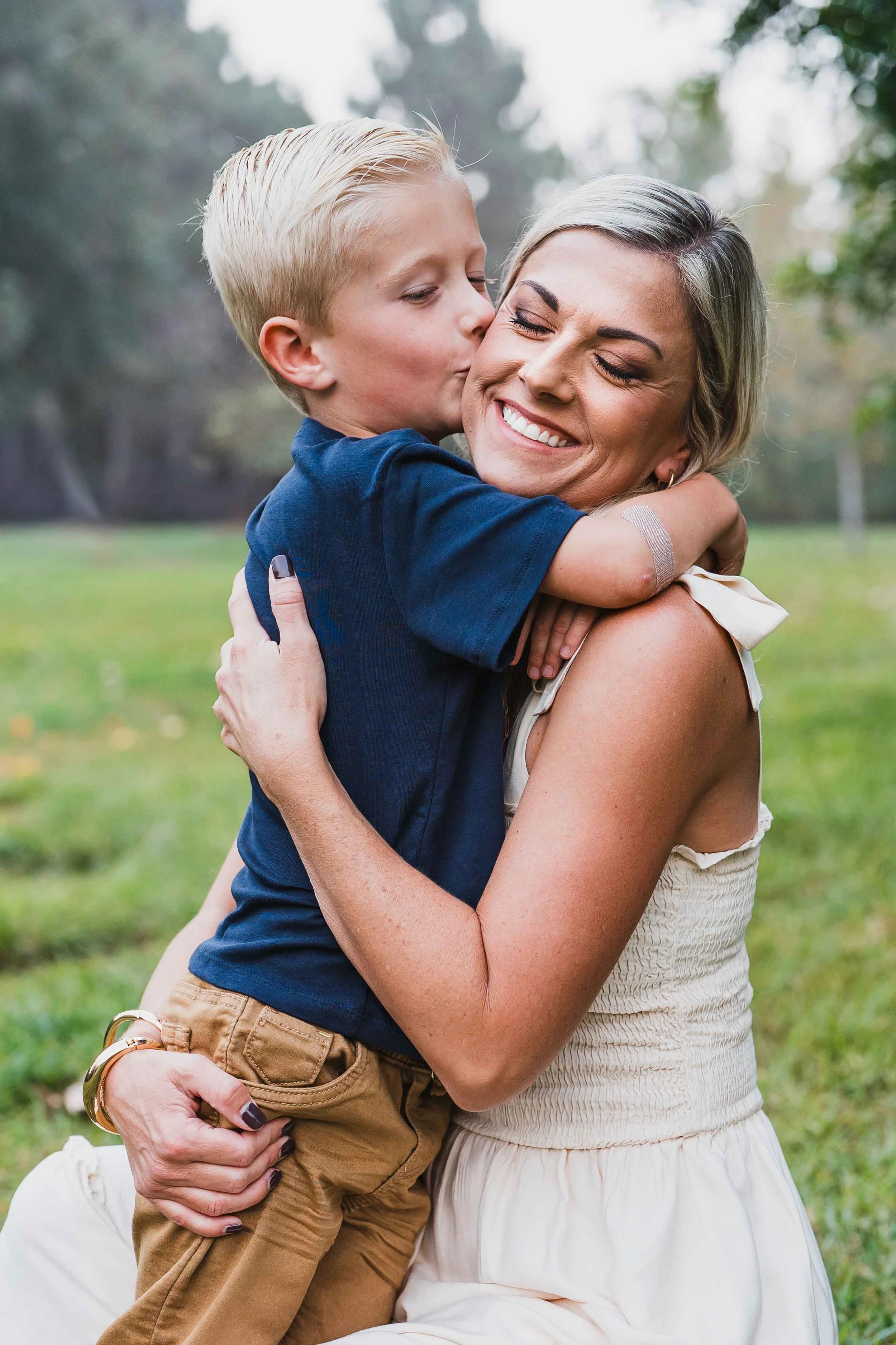 son kissing mom on cheek while mom is kneeling down at park