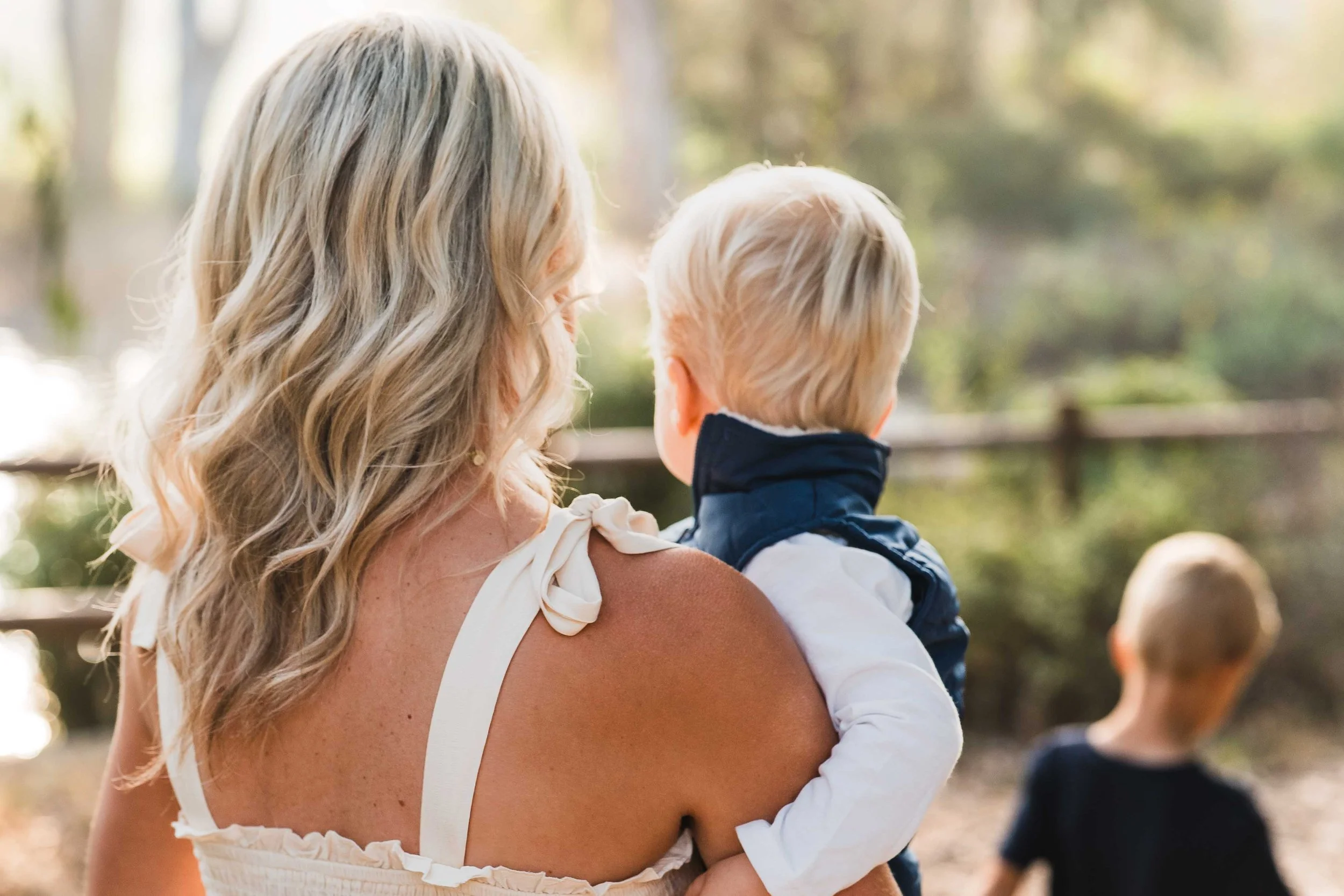 A woman holding a young boy in an outdoor setting with trees in the background.
