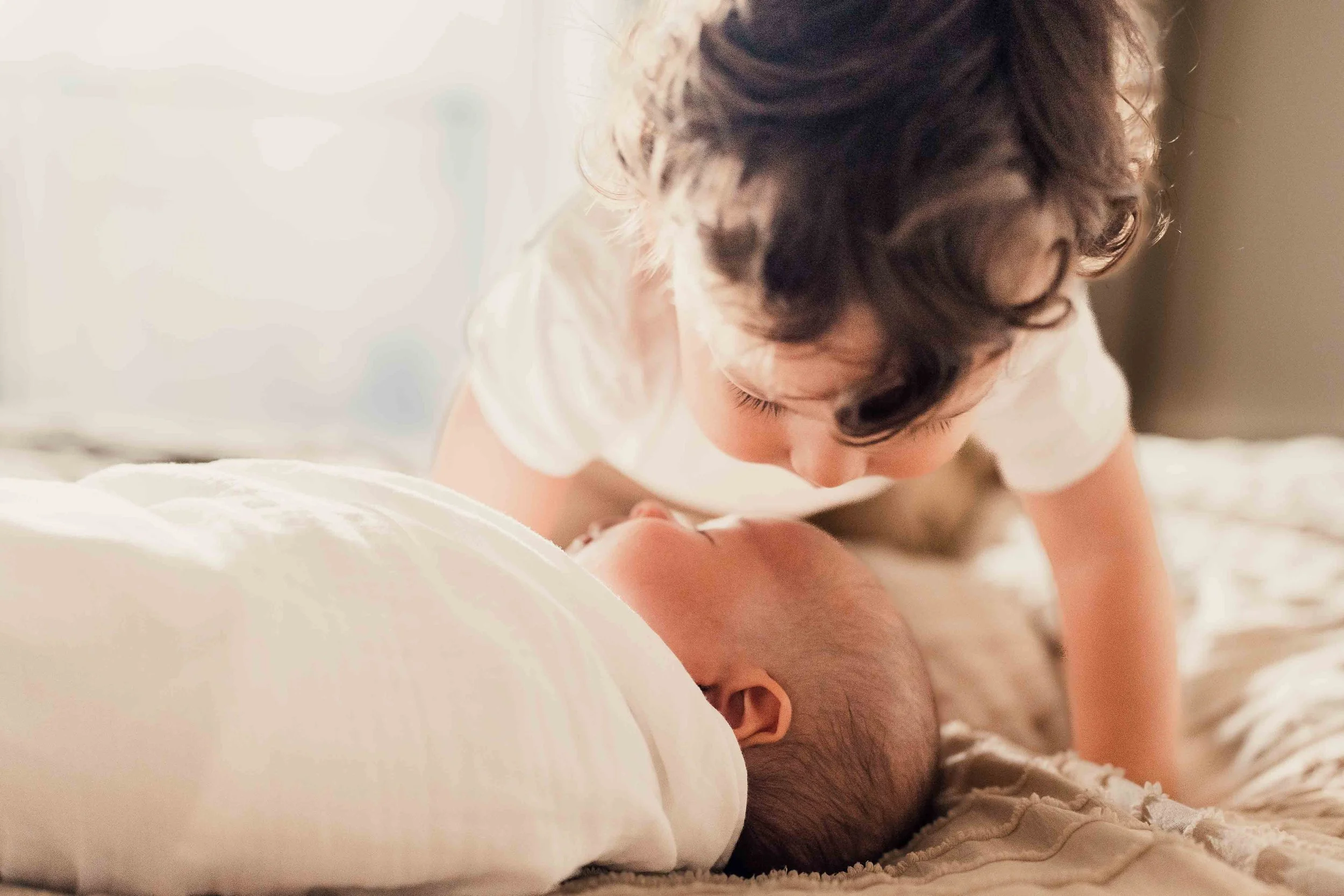 little boy kissing newborn baby on forehead while baby is lying down on bed