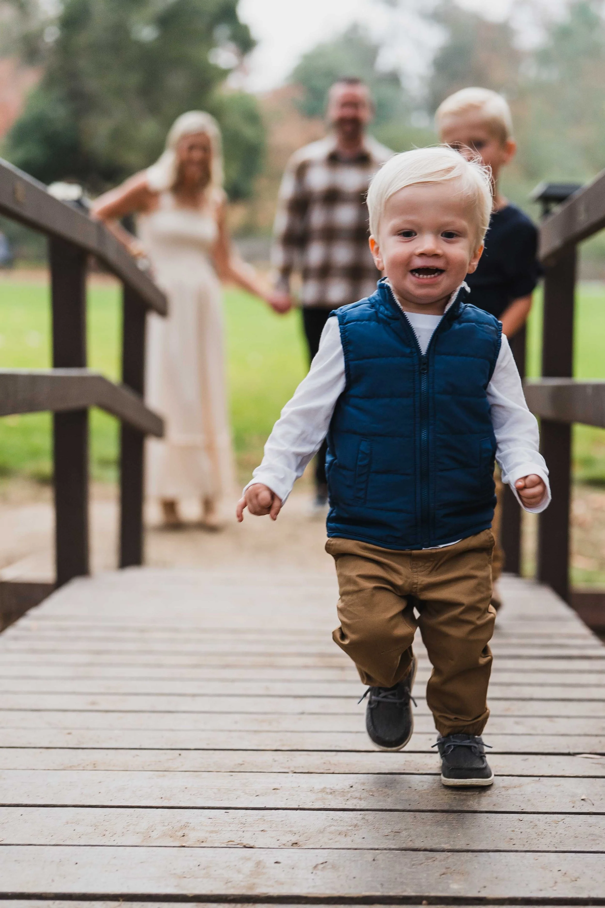 toddler running on small bridge while parents stand in the background