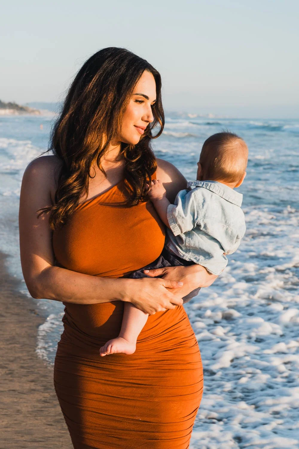 Mom carrying baby walking on dog's beach