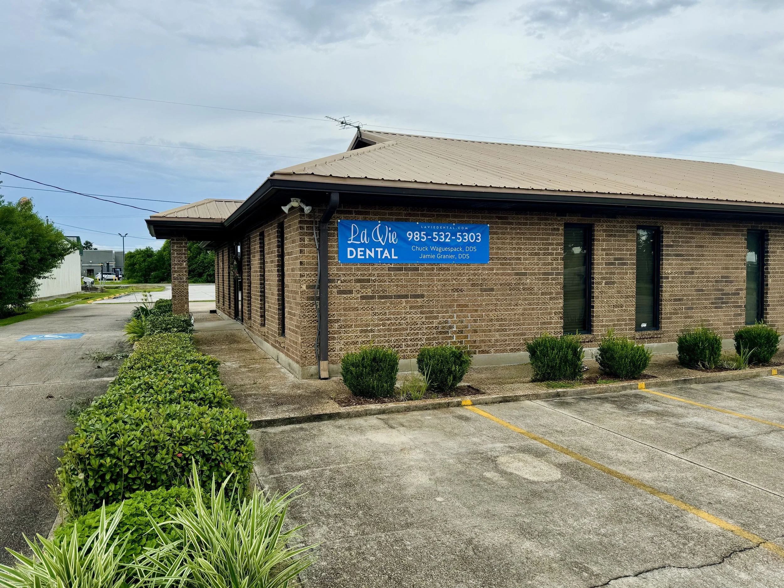 A photograph of the La Vie Dental office on a cloudy day with the company's blue banner featured on its brick wall.