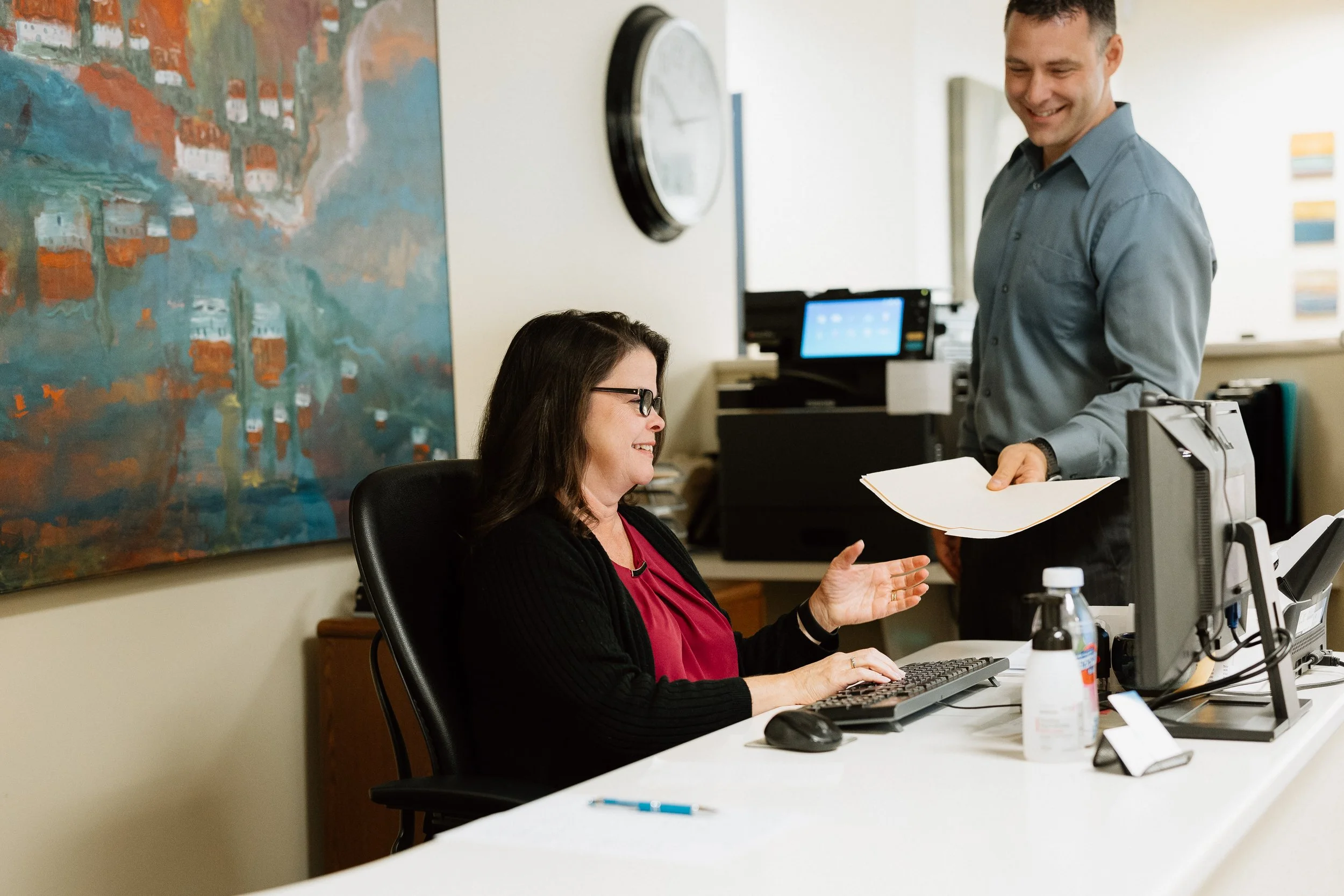 Dr. Opris hands a paper to Marcia sitting at the front desk