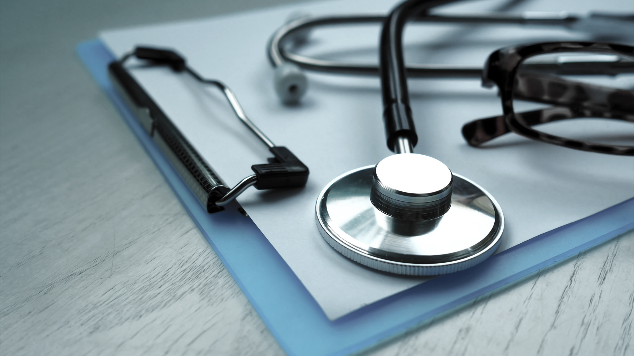 Stethoscope, reflex hammer, and eyeglasses on a clipboard, symbolizing medical care and patient records.