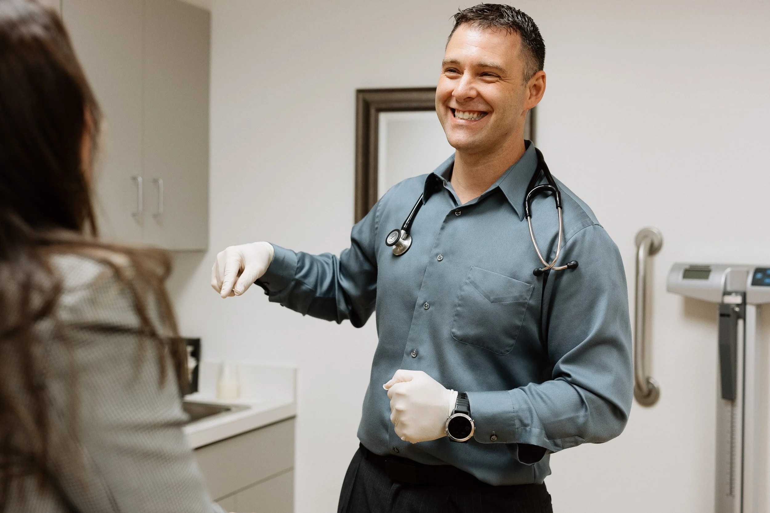 Dr. Opris smiles in an exam room with a stethoscope around his neck and medical gloves on his hands