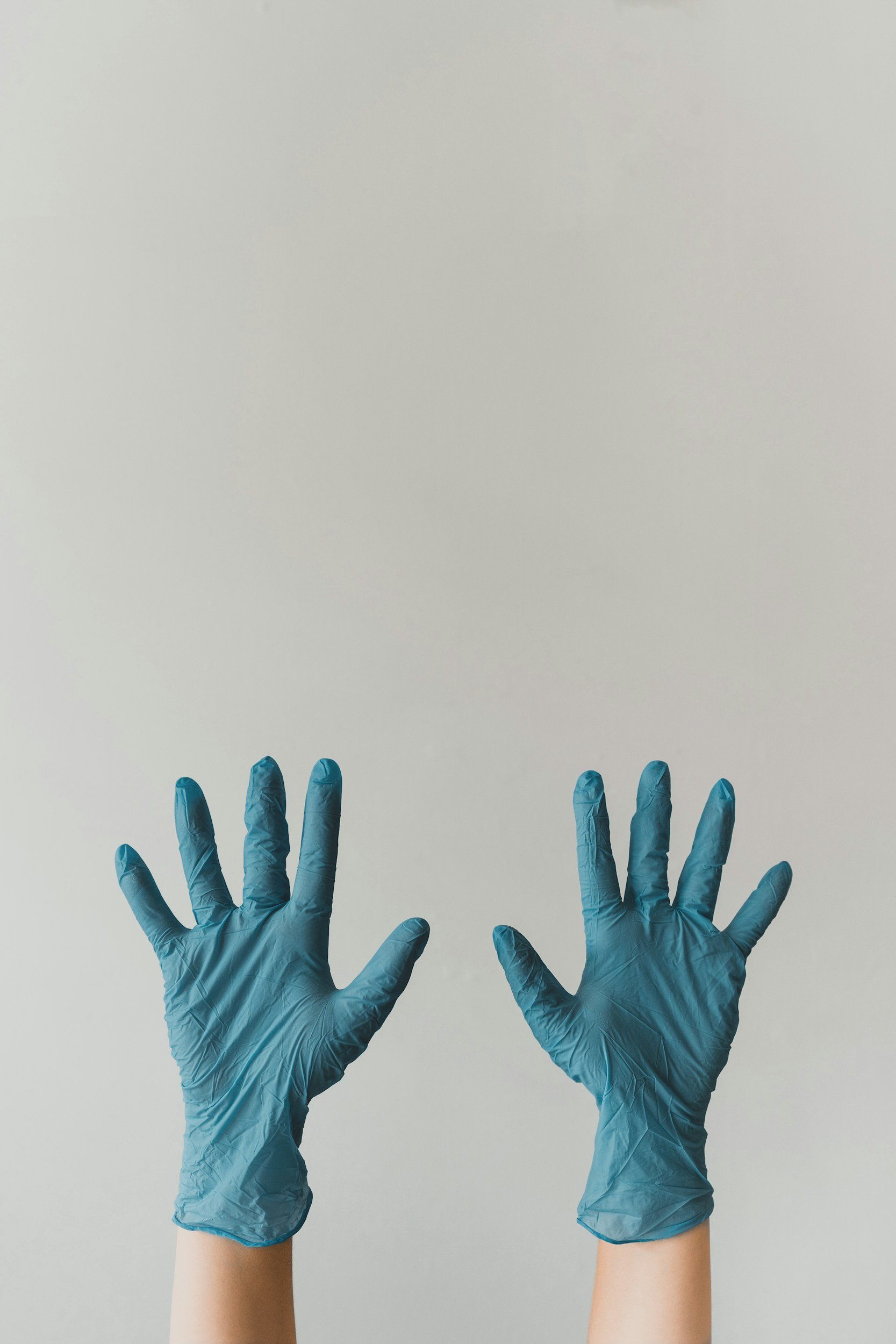 Two hands wearing blue medical gloves are raised against a plain light gray background.