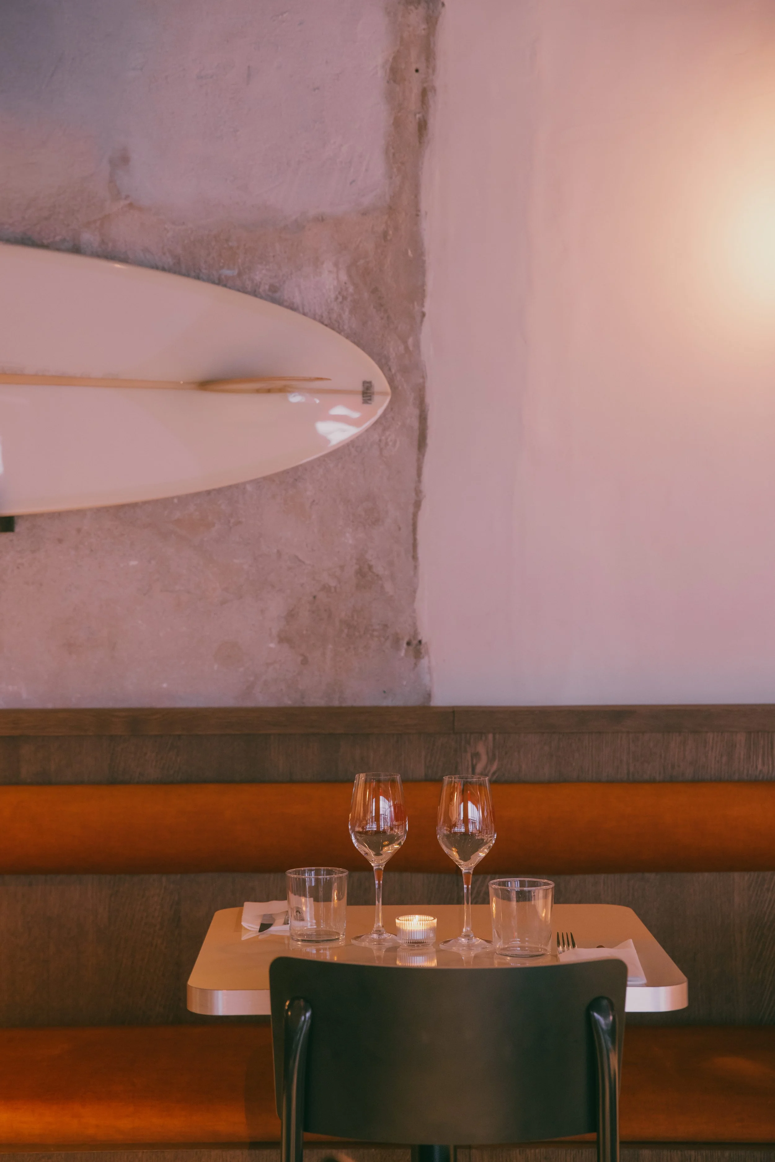 Une table dressée avec deux verres à vin, deux verres d'eau, une bougie et des couverts dans un restaurant avec un mur en pierre et une ambiance chaleureuse.