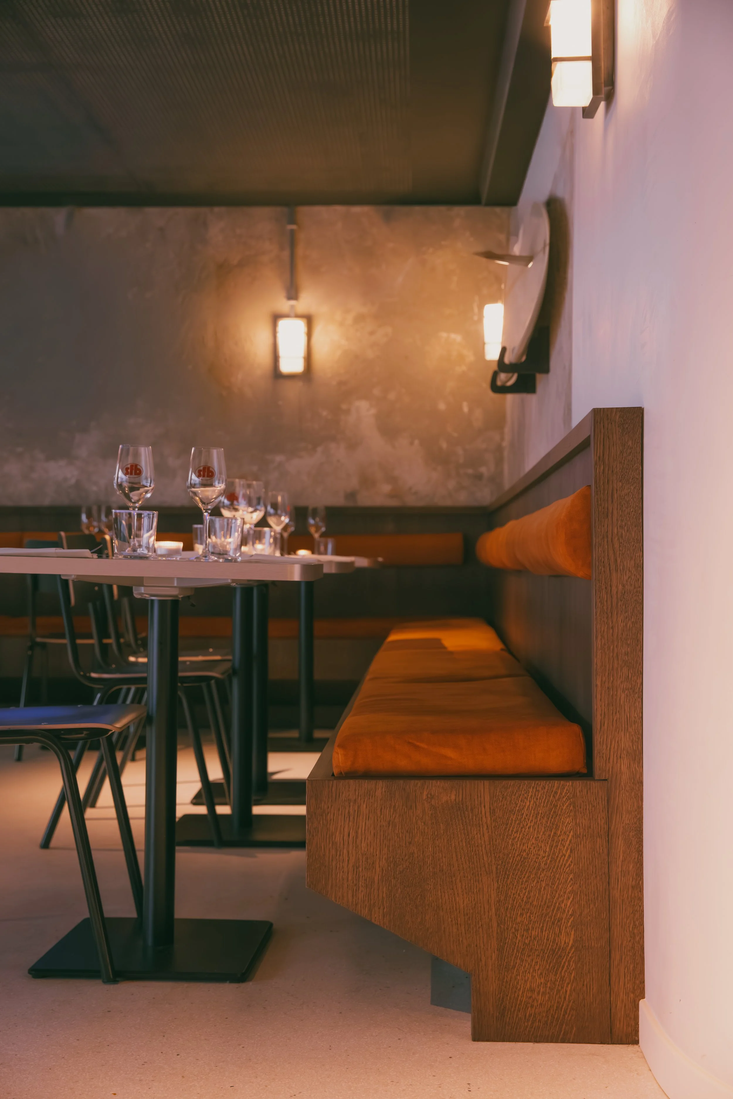 Intérieur d'un restaurant avec une table dressée, plusieurs verres à vin et une banquette en bois avec coussin orange.