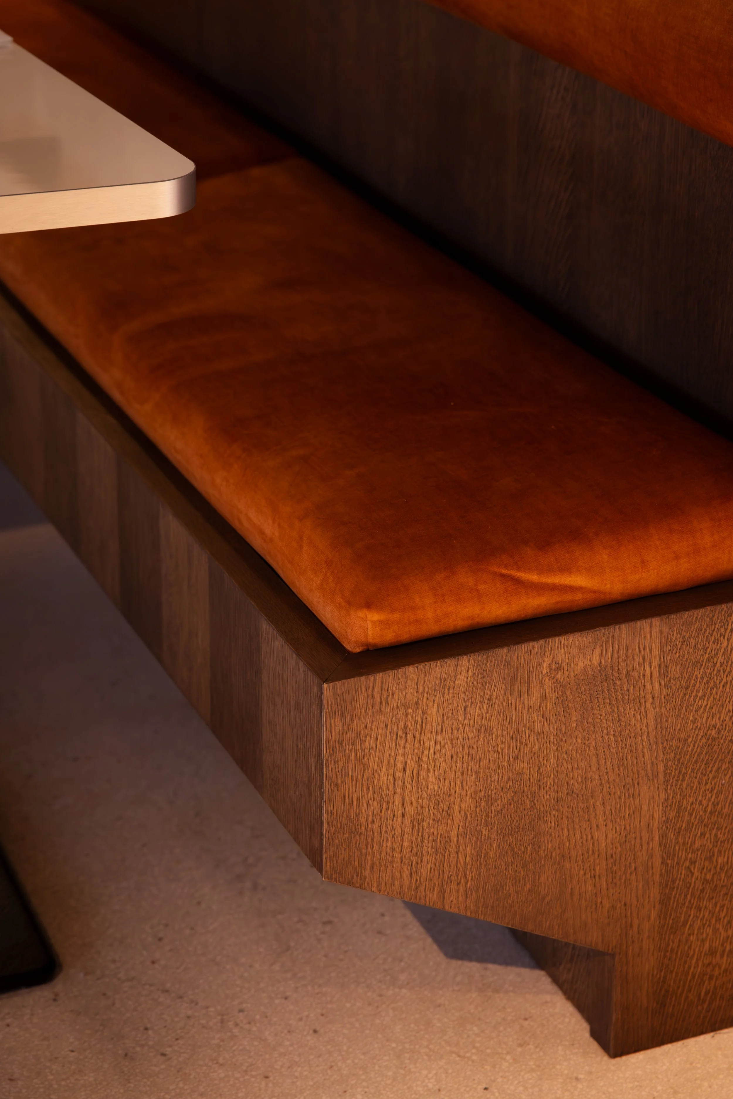 Banquette en bois avec coussin en velours orange dans un intérieur moderne.