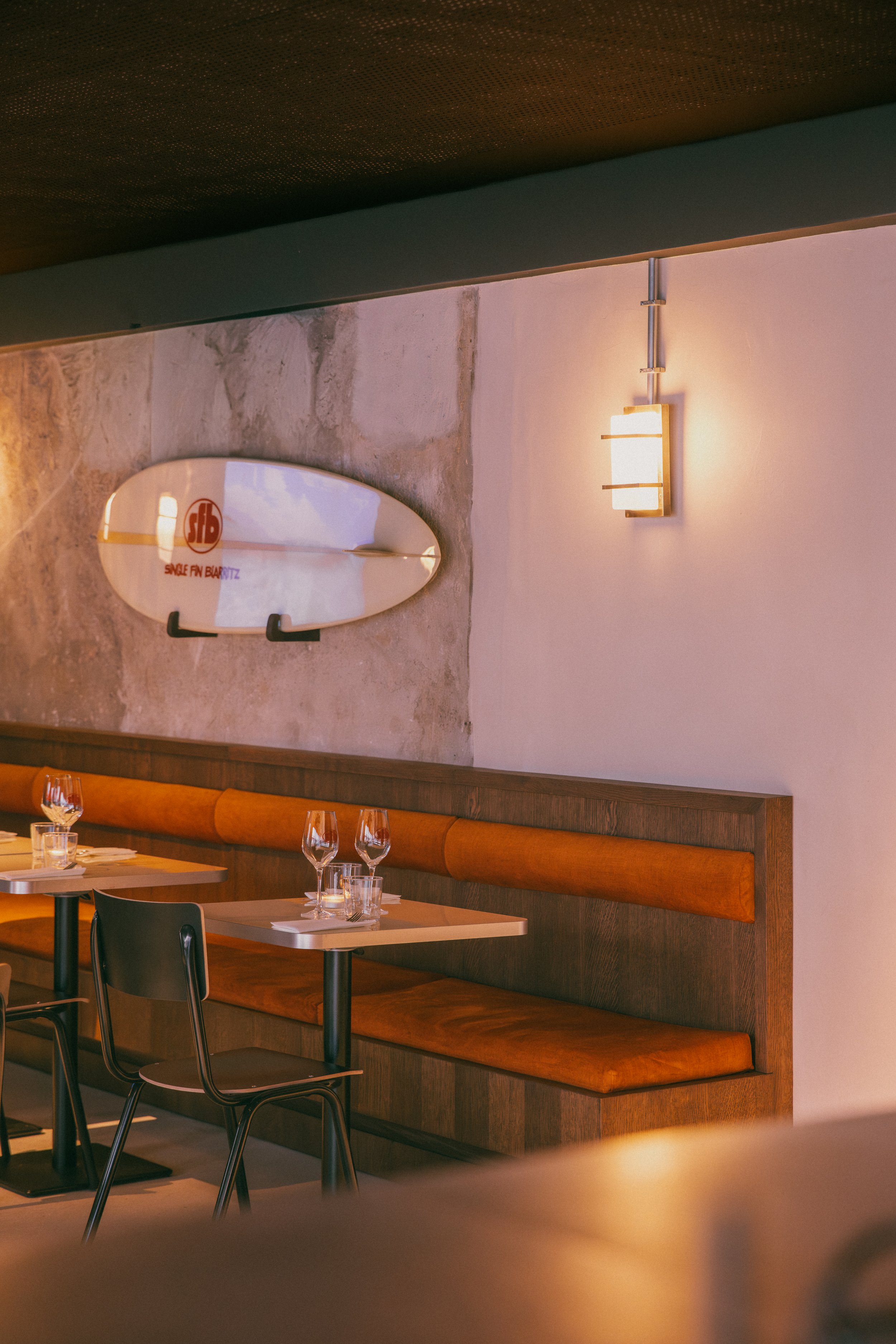 Intérieur de restaurant avec tables, verres à vin, mur en pierre, et une planche de surf suspendue