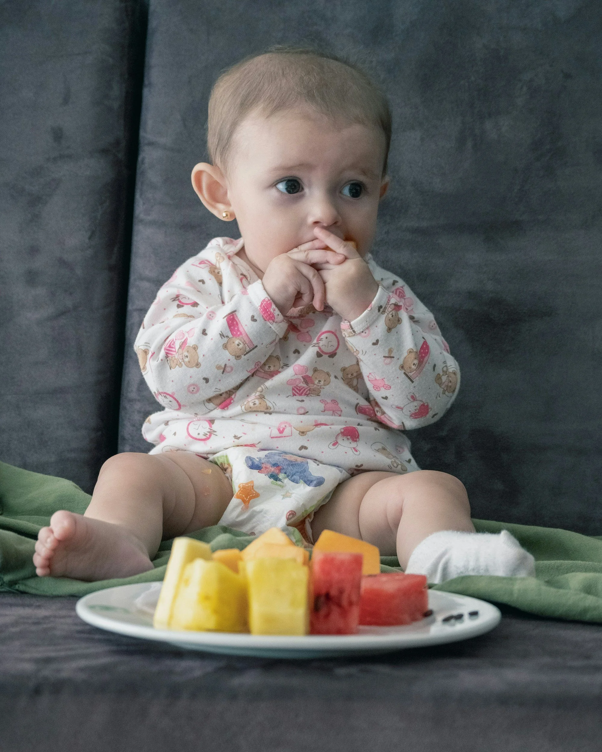 Un bébé assis a des fruits sur une assiette installée devant lui