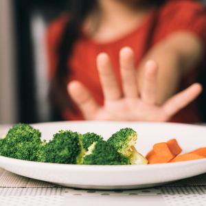 Une petite fille repousse une assiette avec des brocolis et carottes avec sa main