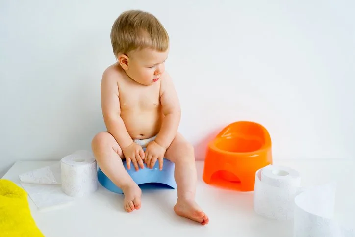 Bébé assis sur un pot et est entouré par un autre pot et papier de toilettes