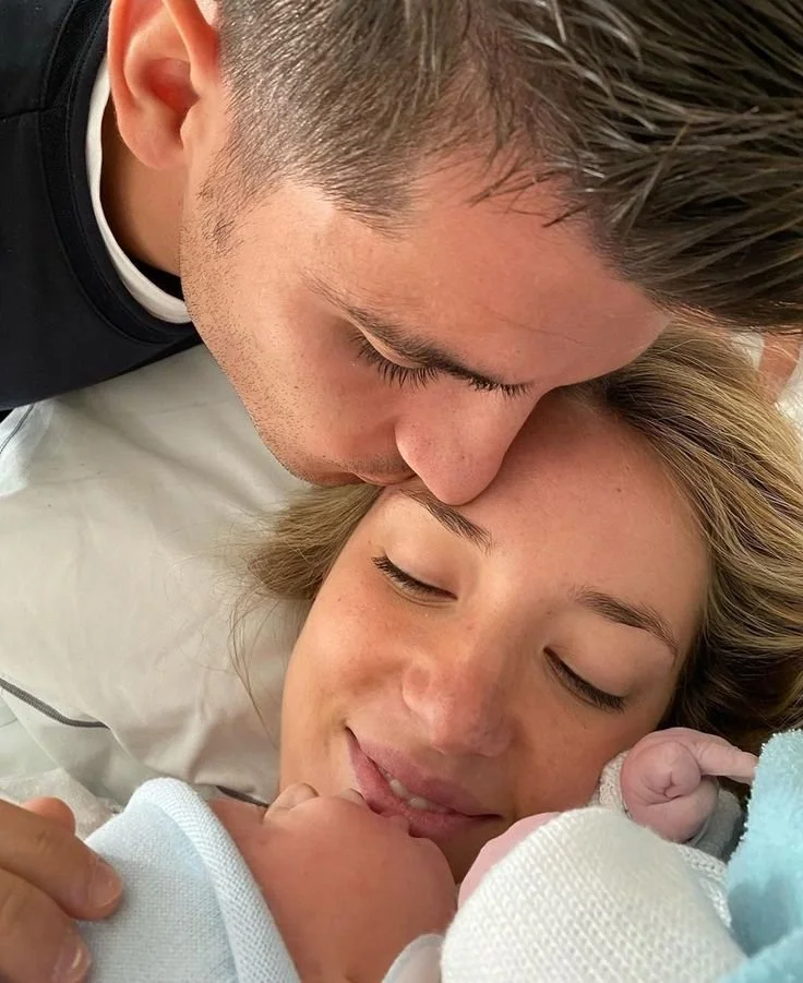 Un couple allongé avec un nouveau-né, le père embrassant la mère.