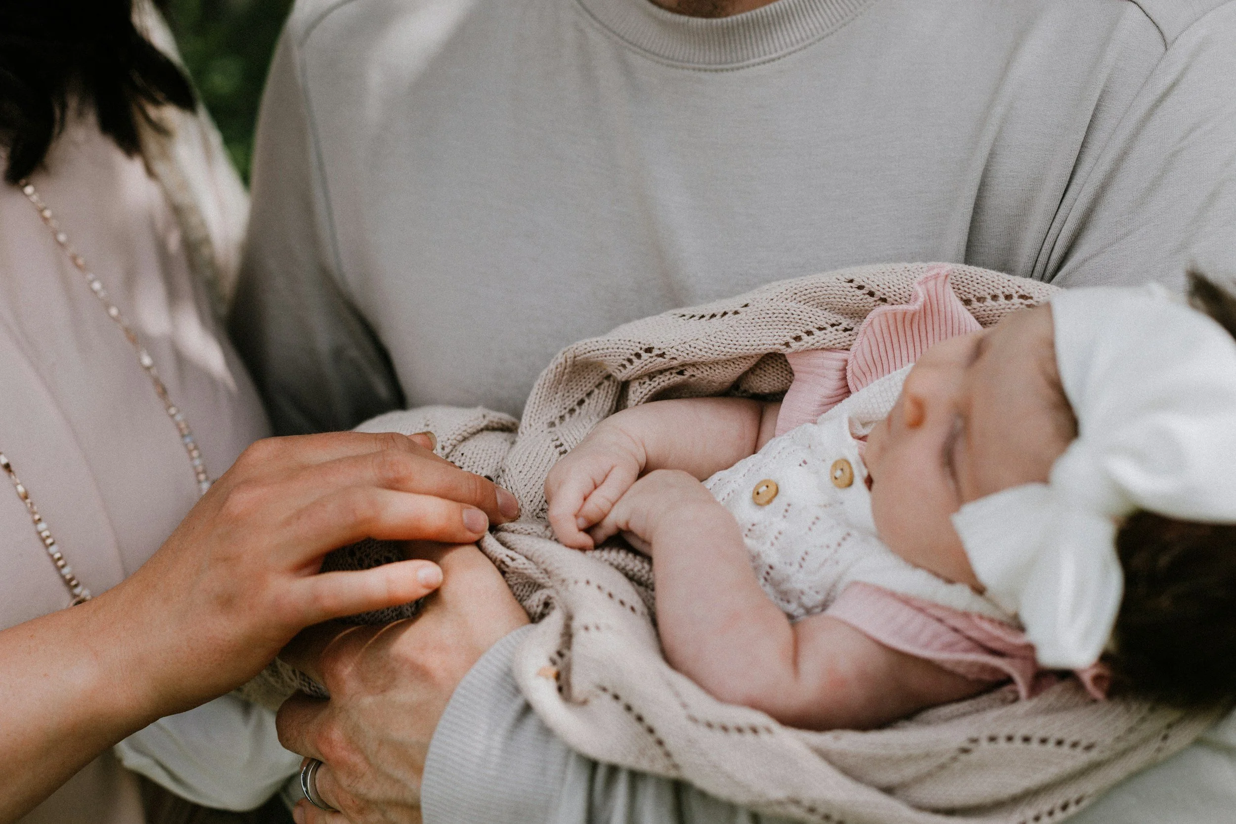 A close-up of a person holding a sleeping baby's tiny hand, with another person's hand gently touching the baby's wrist, in a tender moment.