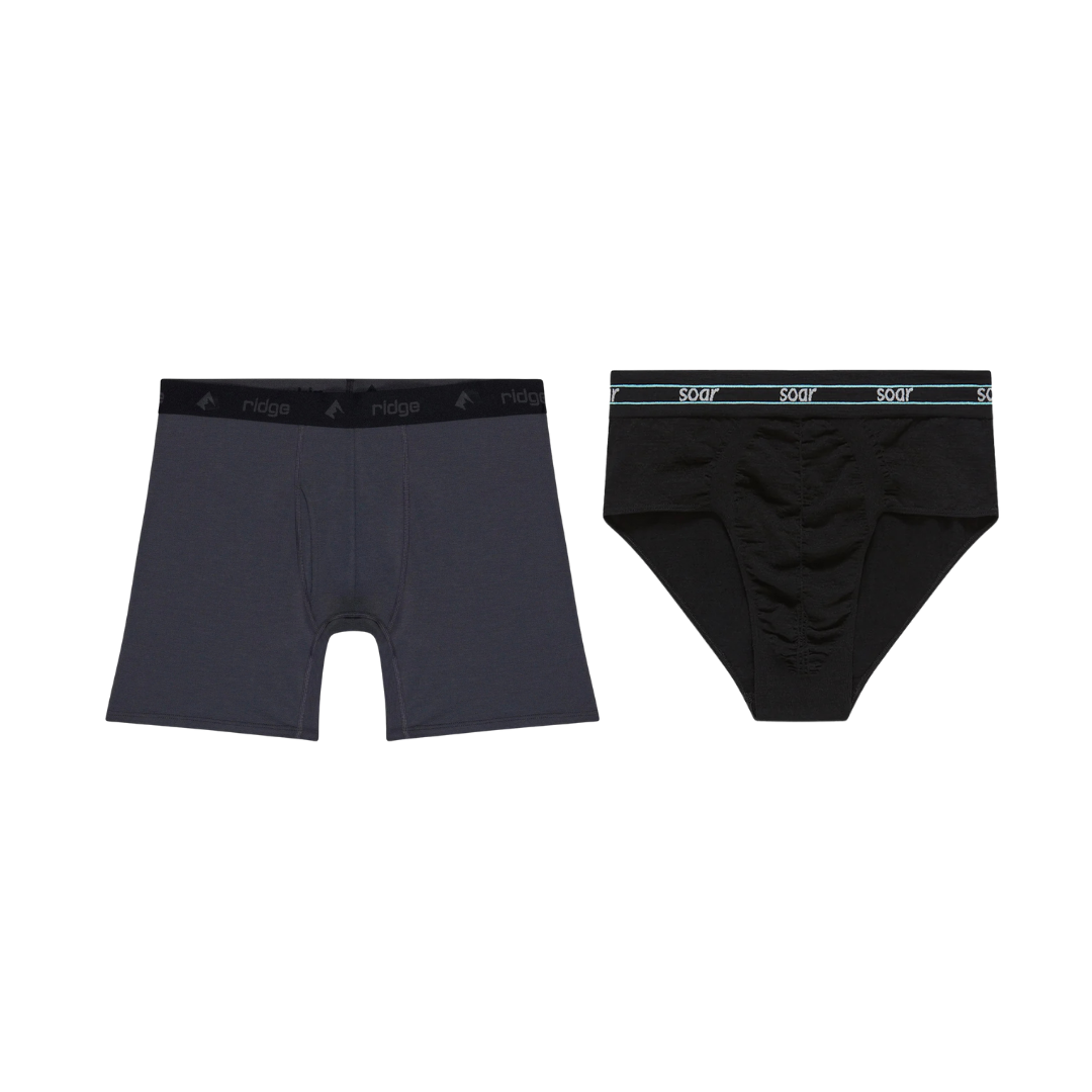 Two men's underwear briefs, one black with teal accents and the word 'soar' on the waistband, and one dark gray with a black waistband and the word 'ridge' on the waistband.