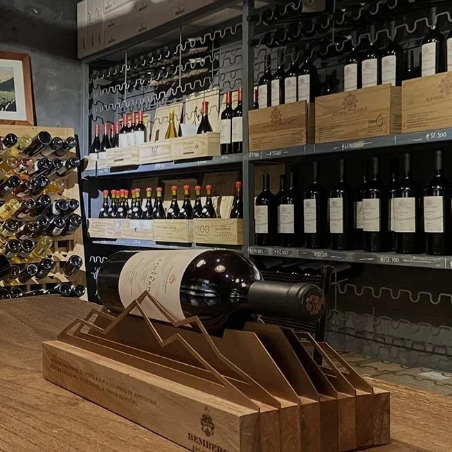 A wine bottle laying on a wooden rack on a table with shelves of wine bottles in a store.