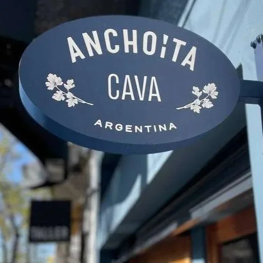 A circular sign that says "Achoíta Cava Argentina" with decorative leaves, hanging outside a building.