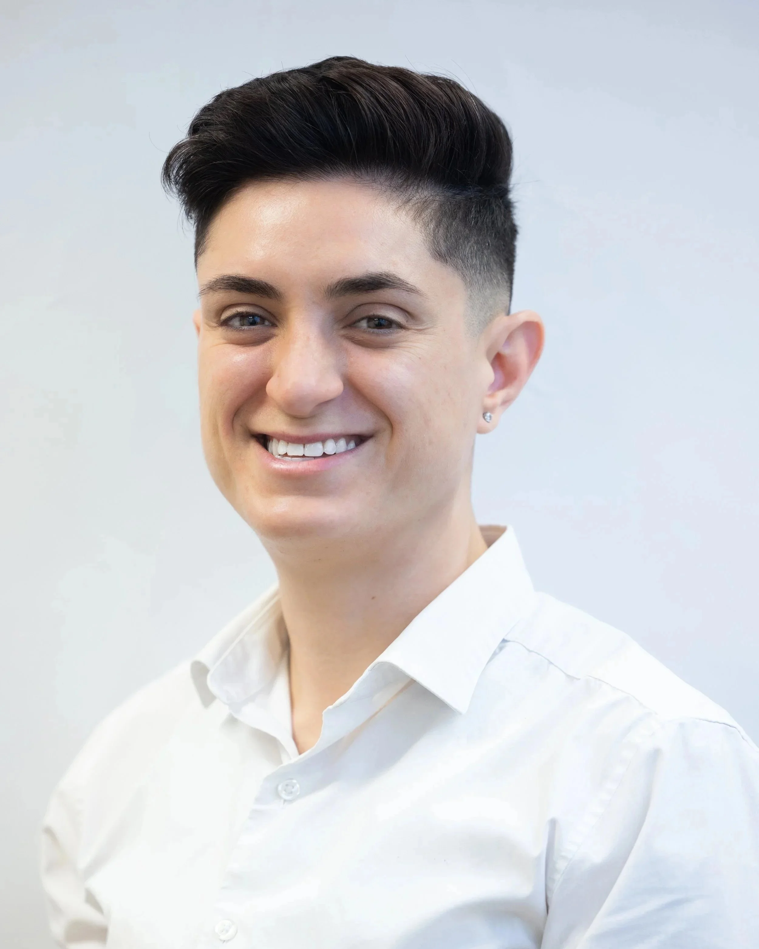 Professional woman with short curly black hair, wearing a white button-up shirt, smiling slightly against a plain white background.